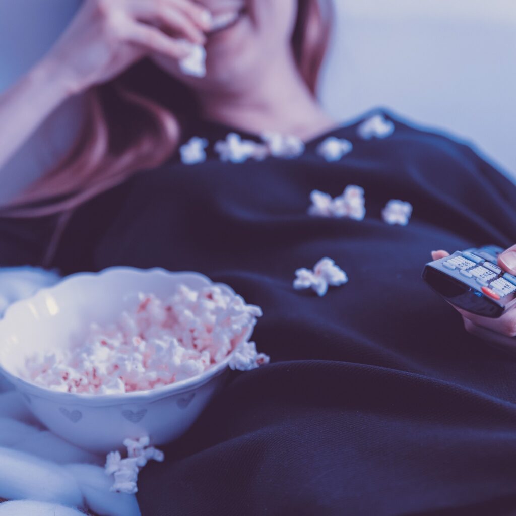 woman watching television on couch with popcorn