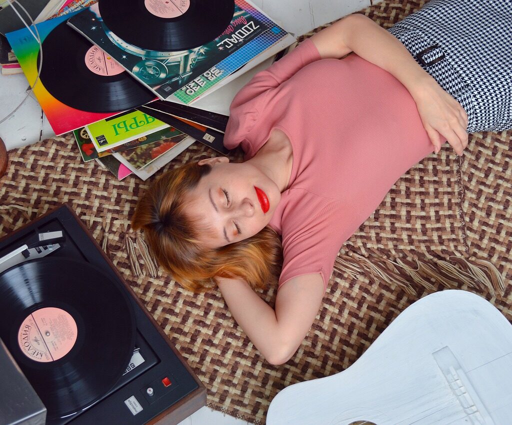 red head girl with red lipstick laying on bed listening to record