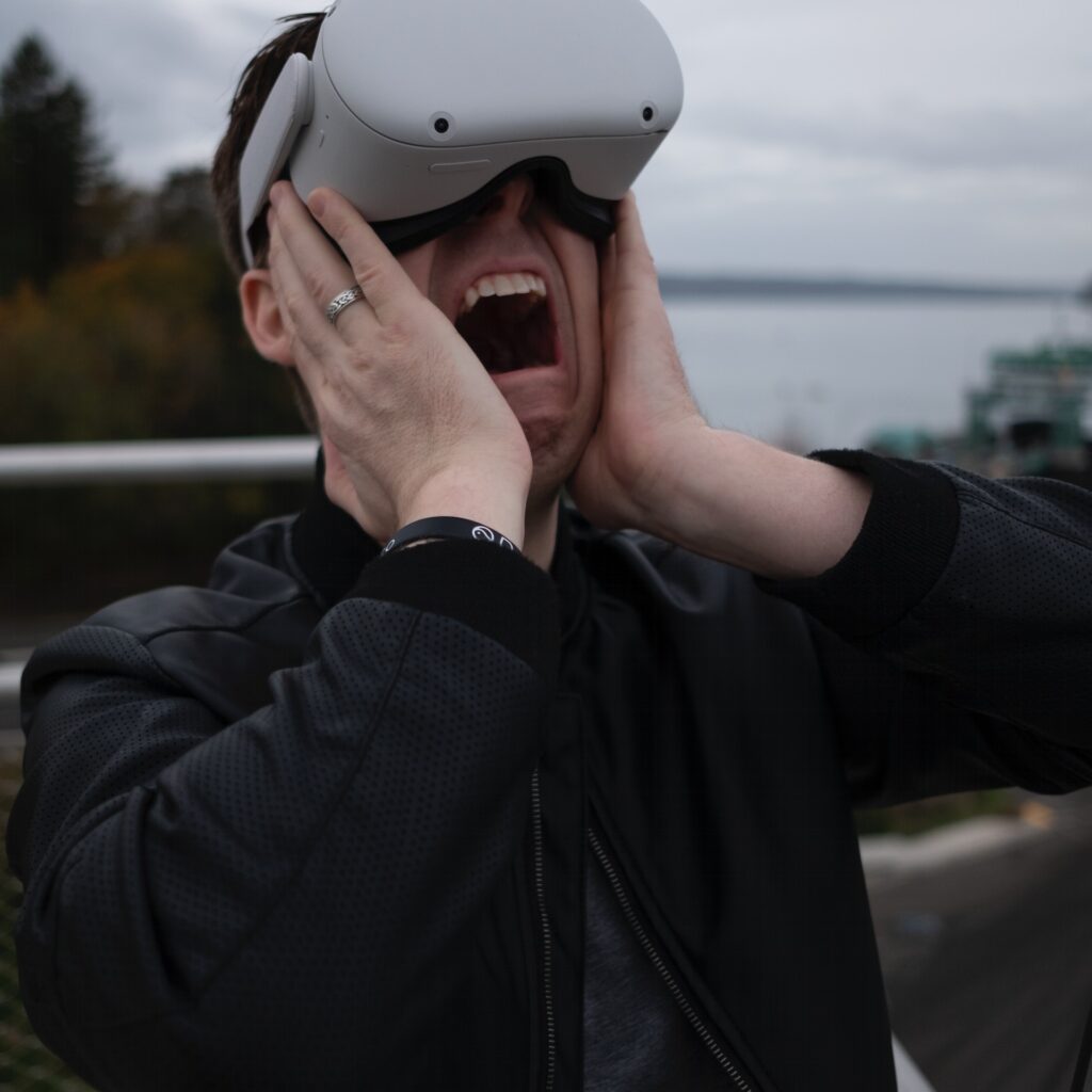 Man wearing VR goggles clasping his hand to his face screaming at the VR horror game.