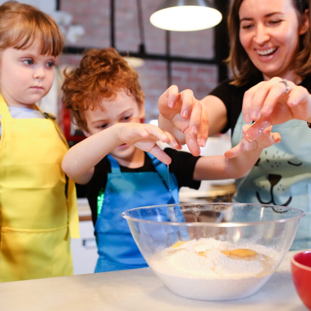 two kids at a community cooking class. They are sprinkling sugar into a mixing bowl.