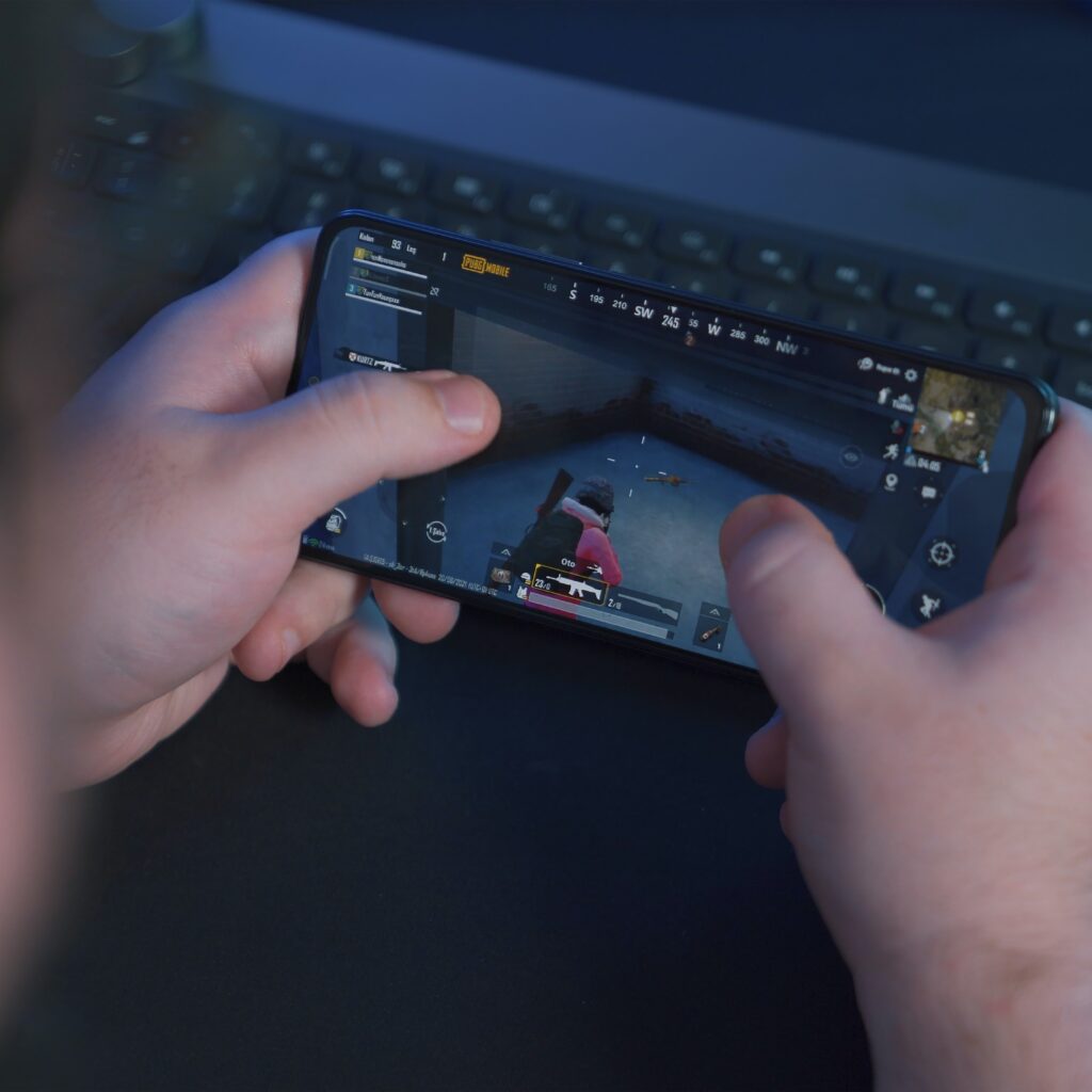 A person holding a phone sideways. The game displayed on the screen is PUBG Mobile. 