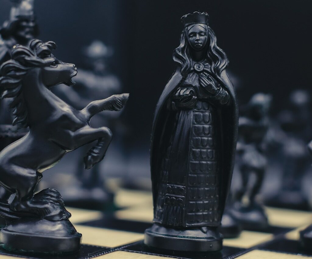 An up-close shot of a queen chess piece and knight chess game pieces.