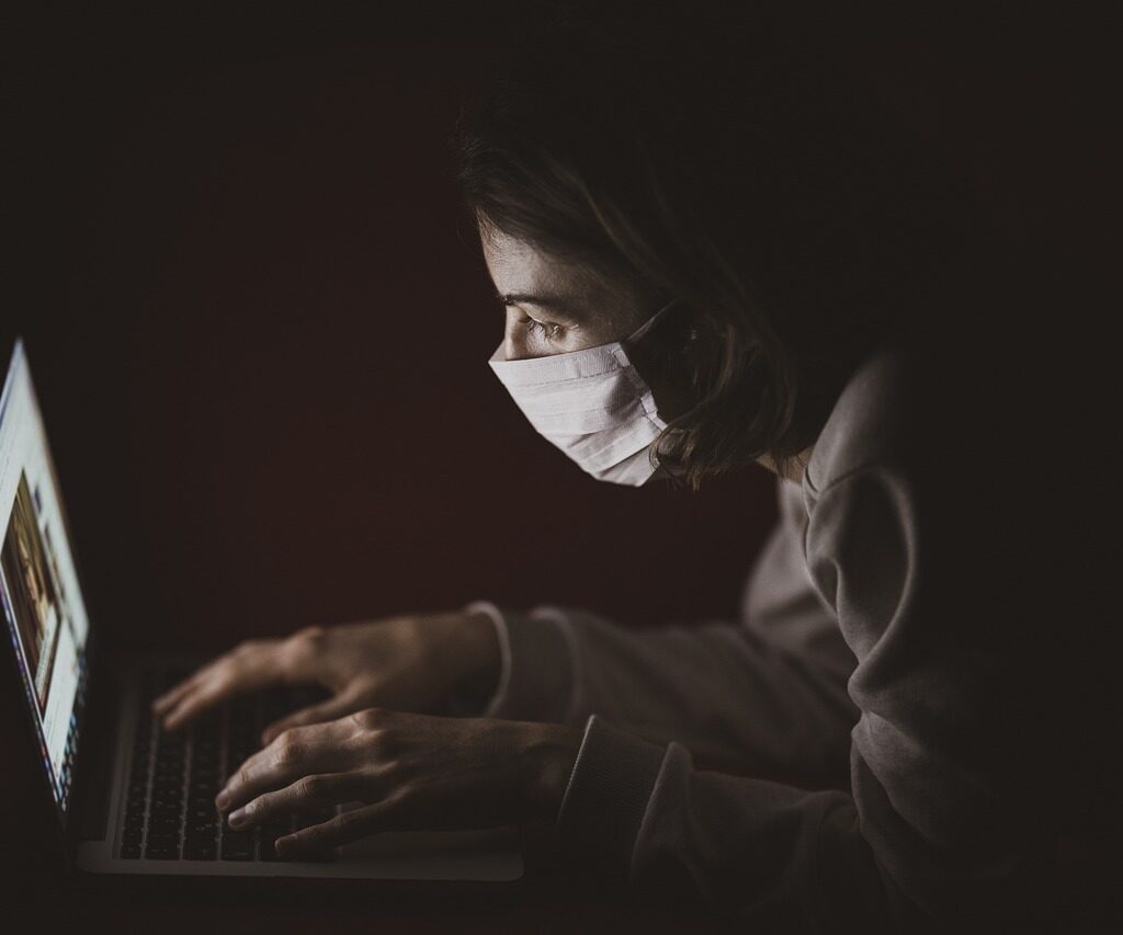 A person wearing a face mask is watching a video on a laptop,