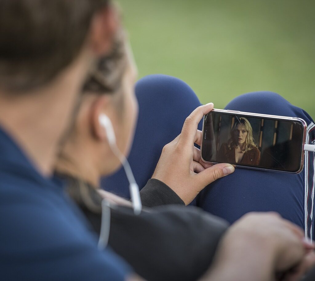 A man and a woman sit watching something on a smartphone. 