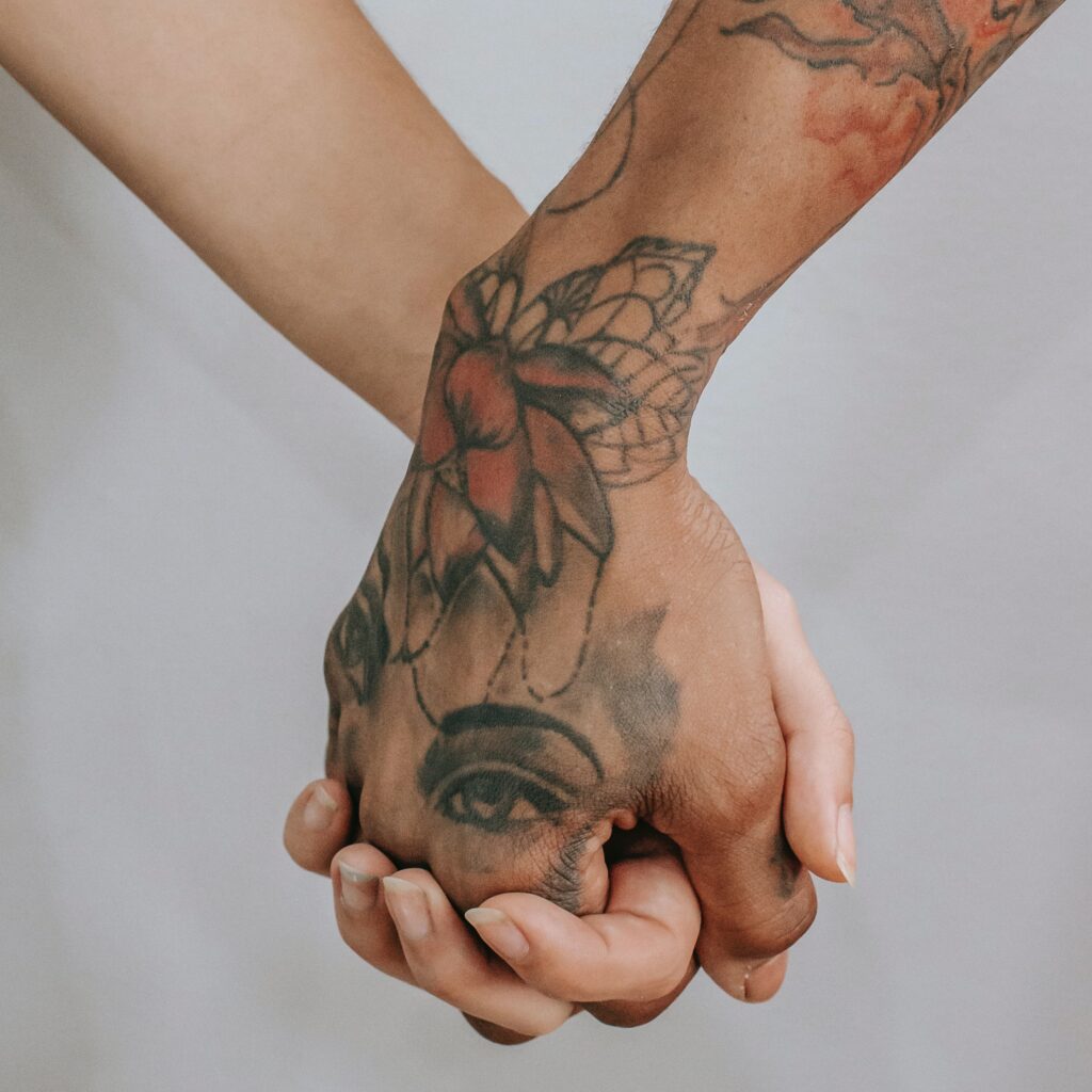 Two people holding hands. One of the hands has a tattoo and the other does not. 