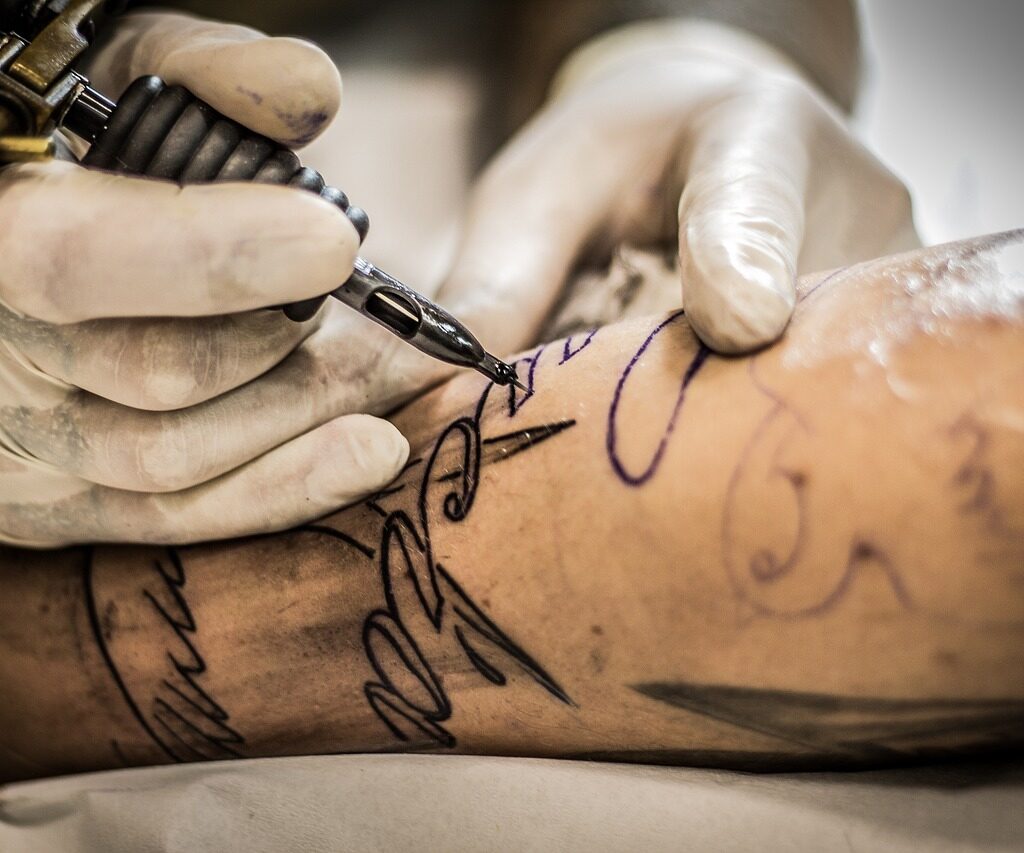 A tattoo artist tattooing an arm. 