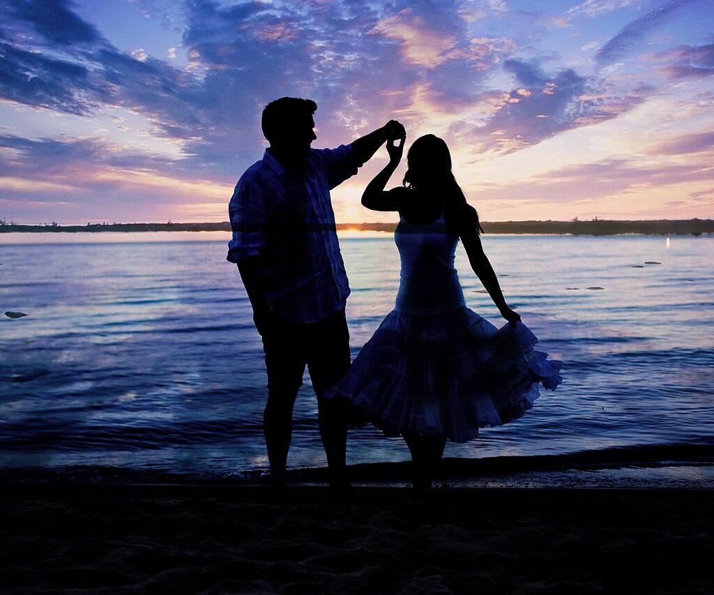 A couple dancing at the beach during the sunset.