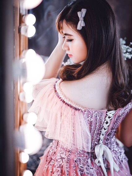 Girl wearing a pink dress with ruffles and bow in hair, of seeming lolita fashion.