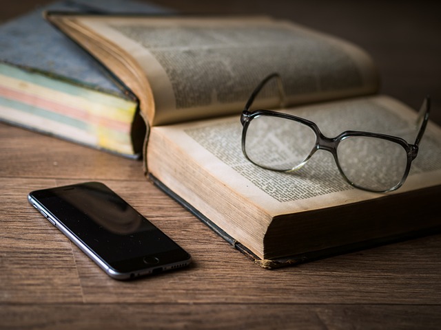 Glasses resting on book next to phone on table. Representative of visual novel.