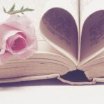 Book pages formed to shape a heart with rose beside it. In article about visual novel games.