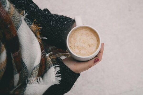 Someone holding a white cup of hot chocolate in their hands.