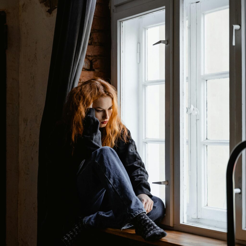 Girl learning her head on her hand while sitting on a windowsil.