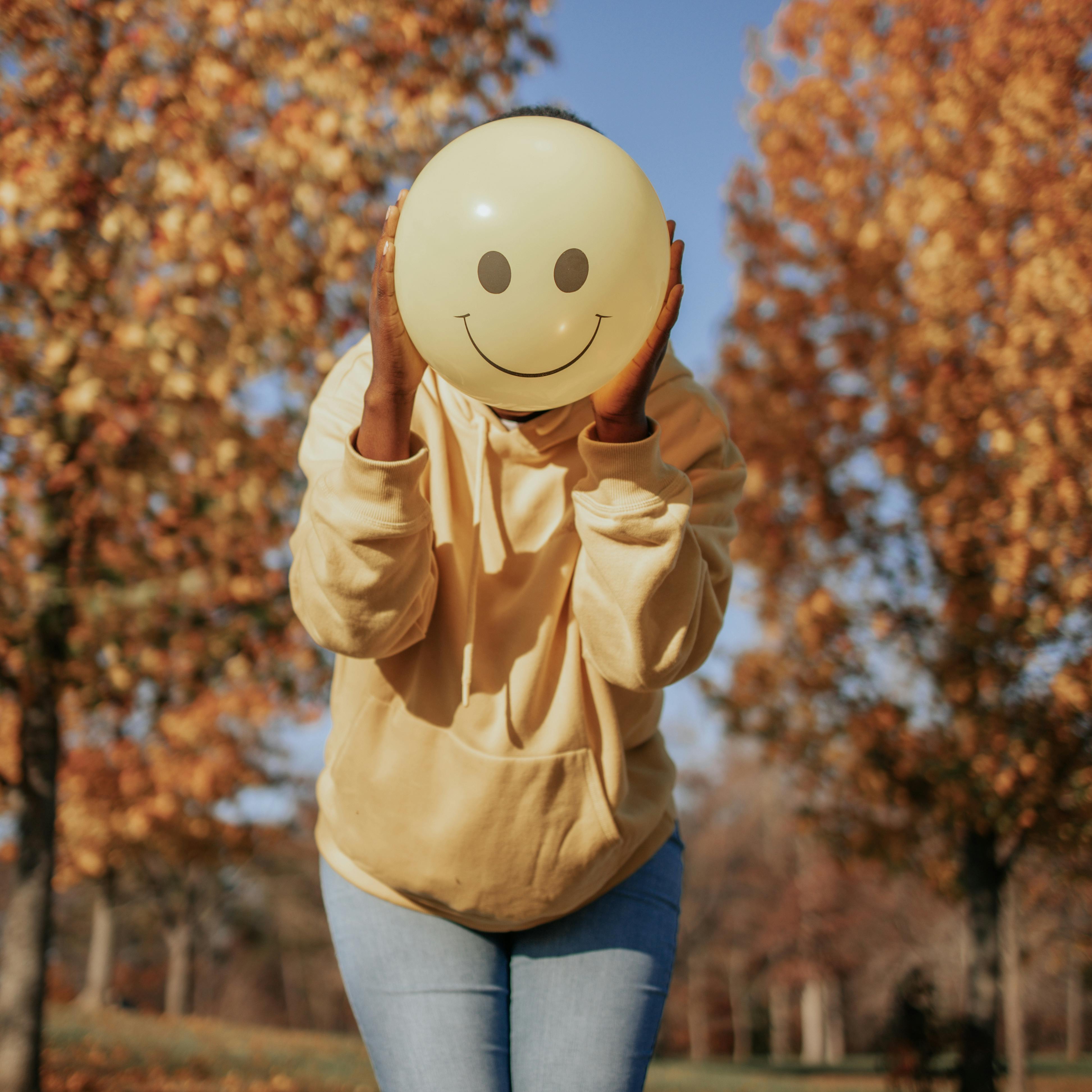  A person masking their face with a balloon that has a smile over it