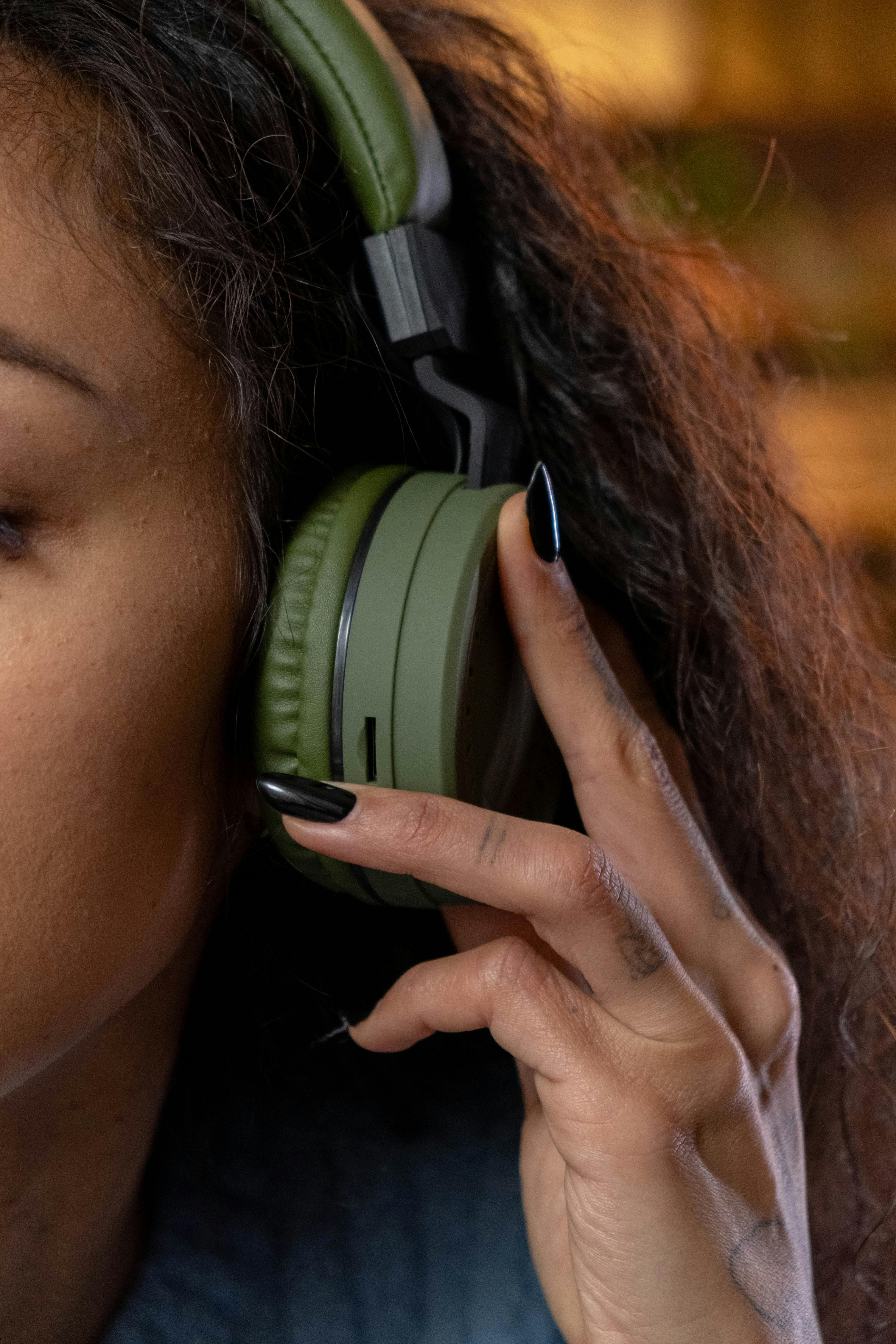 Close-up of a person wearing noise-canceling headphones, eyes closed, appearing calm and relaxed while listening to music in a softly lit room.