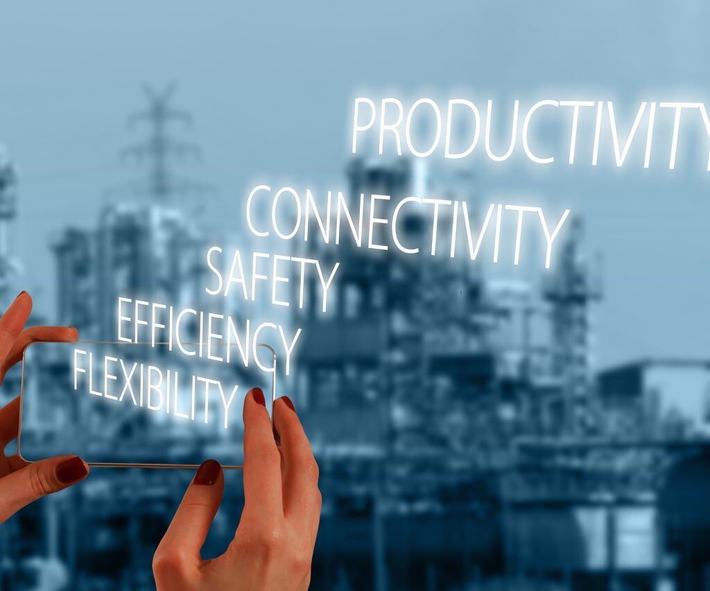 Hands holding a phone with glowing text reading productivity, connectivity, safety, efficiency, and flexibility over an industrial background